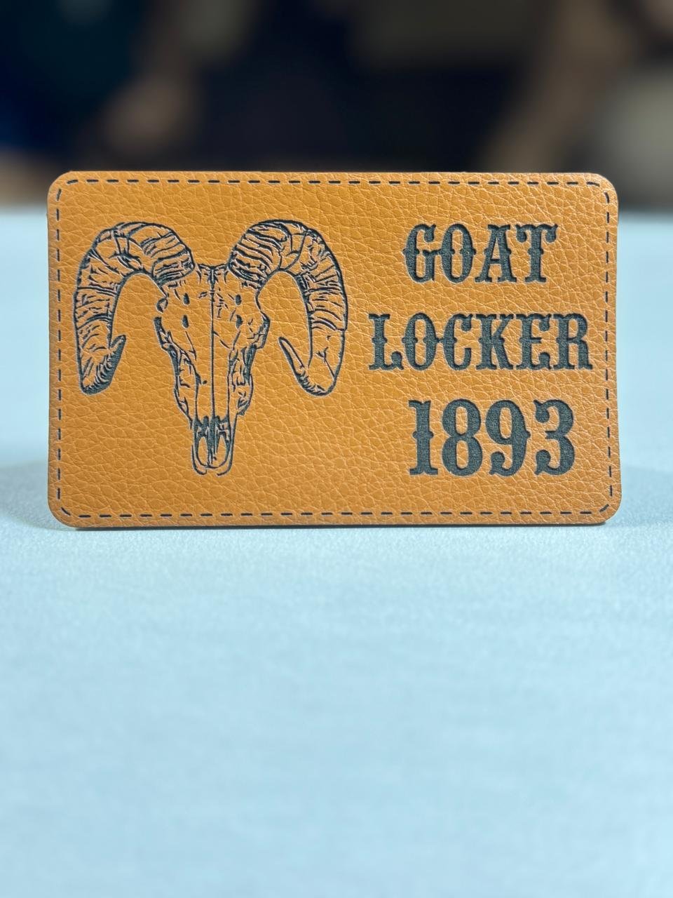 Brown laser engraved Goat Locker 1893 leatherette patch featuring a ram skull design with custom text and stitched border for tactical gear and personalised accessories. Custom Tactical Name Patch